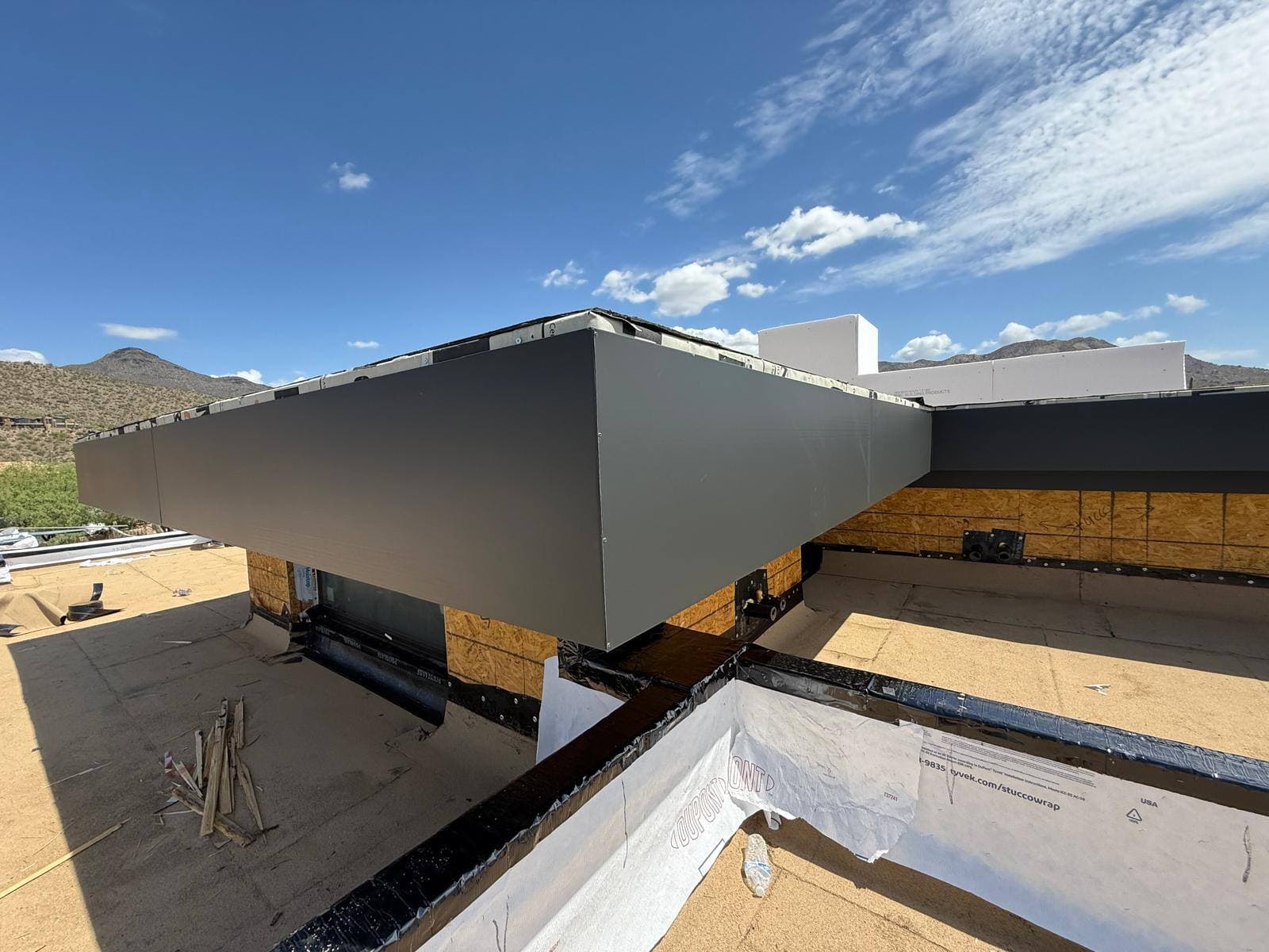 Cantilevered roof wing wrapped in gray metal fascia projecting over a flat granulated roof deck with freshly flashed parapet base.