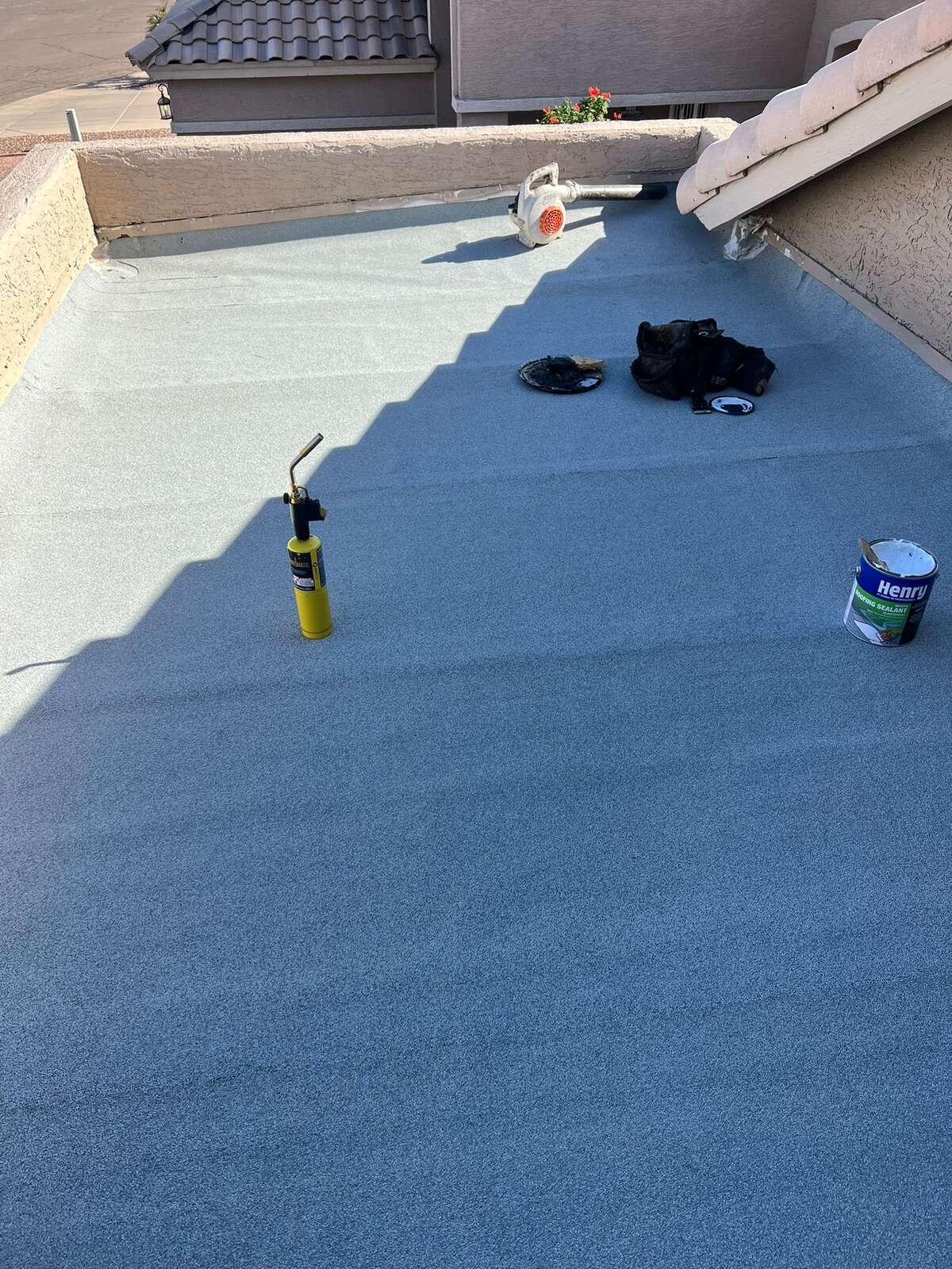 A low-slope residential roof finished with gray granulated cap sheet, with a propane torch, blower and roofing sealant staged across the deck.