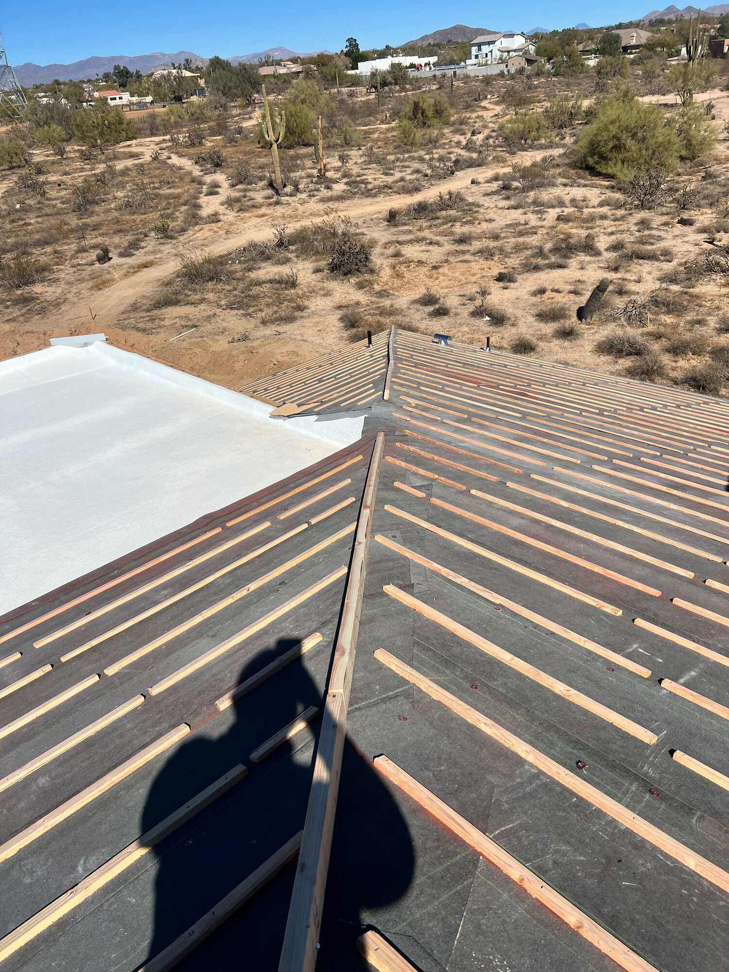Roof battens laid over underlayment on a custom desert home under a deep blue sky with mountains on the horizon