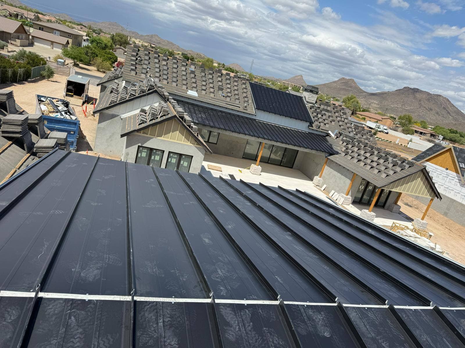 New desert home under construction with black standing seam metal panels laid and roof tile stacked across adjacent slopes