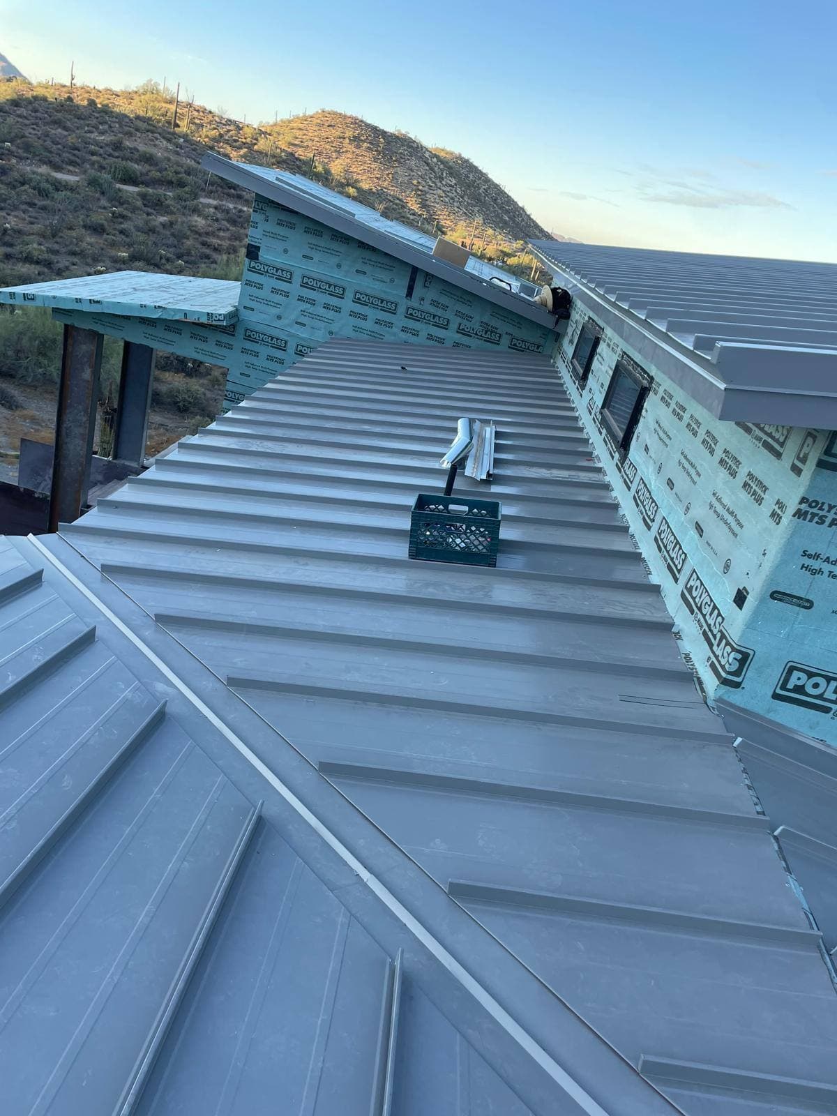 New-construction desert modern home with light gray standing-seam metal roof panels installed and parapet walls still in self-adhered underlayment