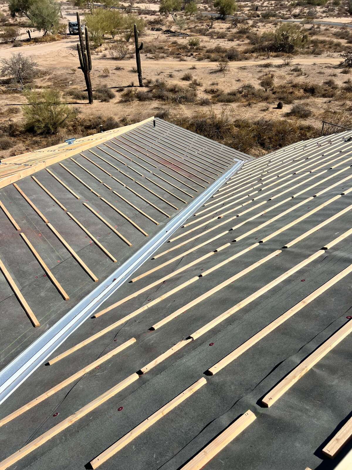 New-construction roof deck with black underlayment and fresh wood battens meeting at a metal-lined valley, overlooking Sonoran desert
