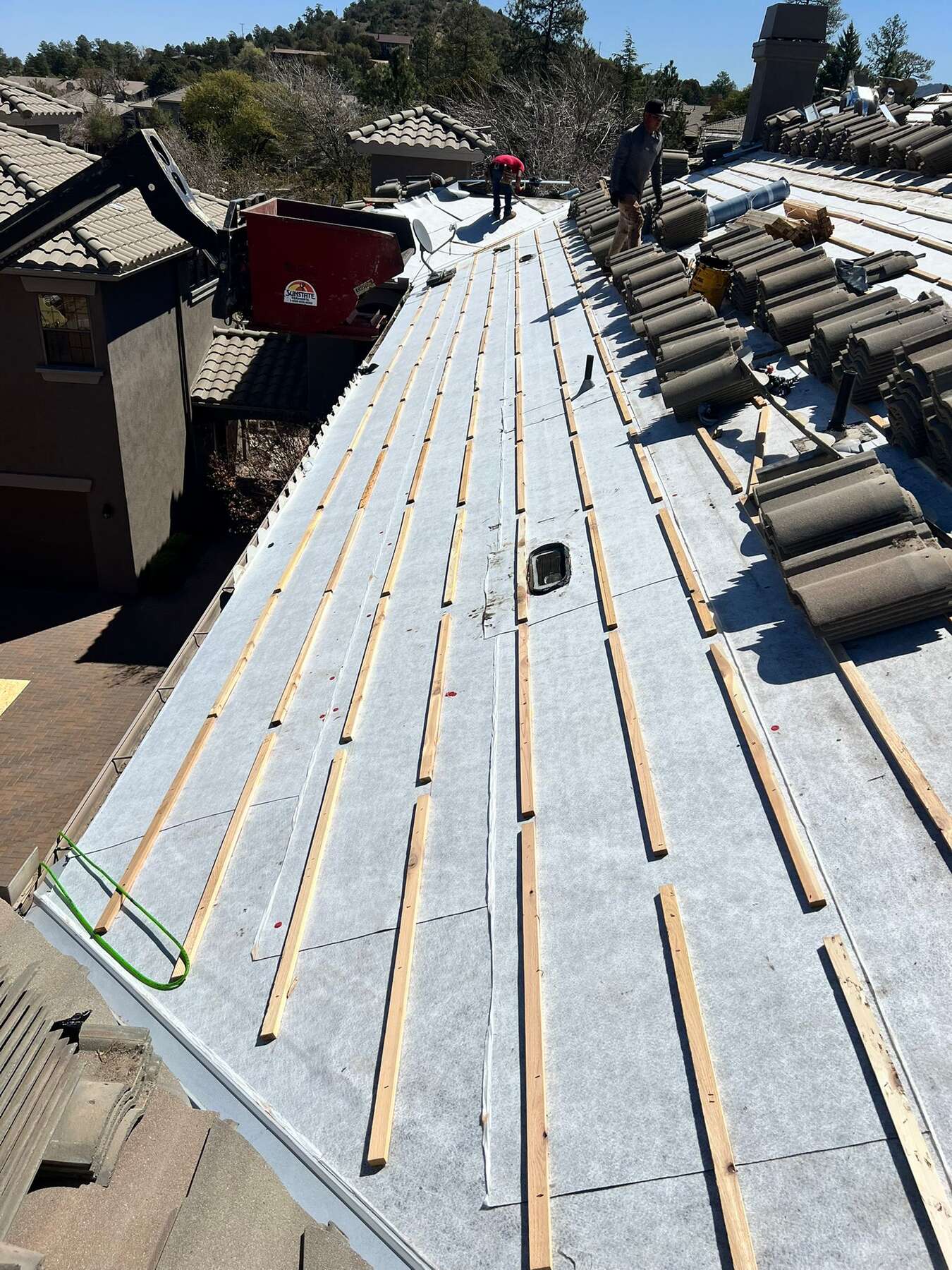 Tile re-roof in progress with fresh white underlayment, wood battens and stacked concrete tile being loaded onto the adjacent slope