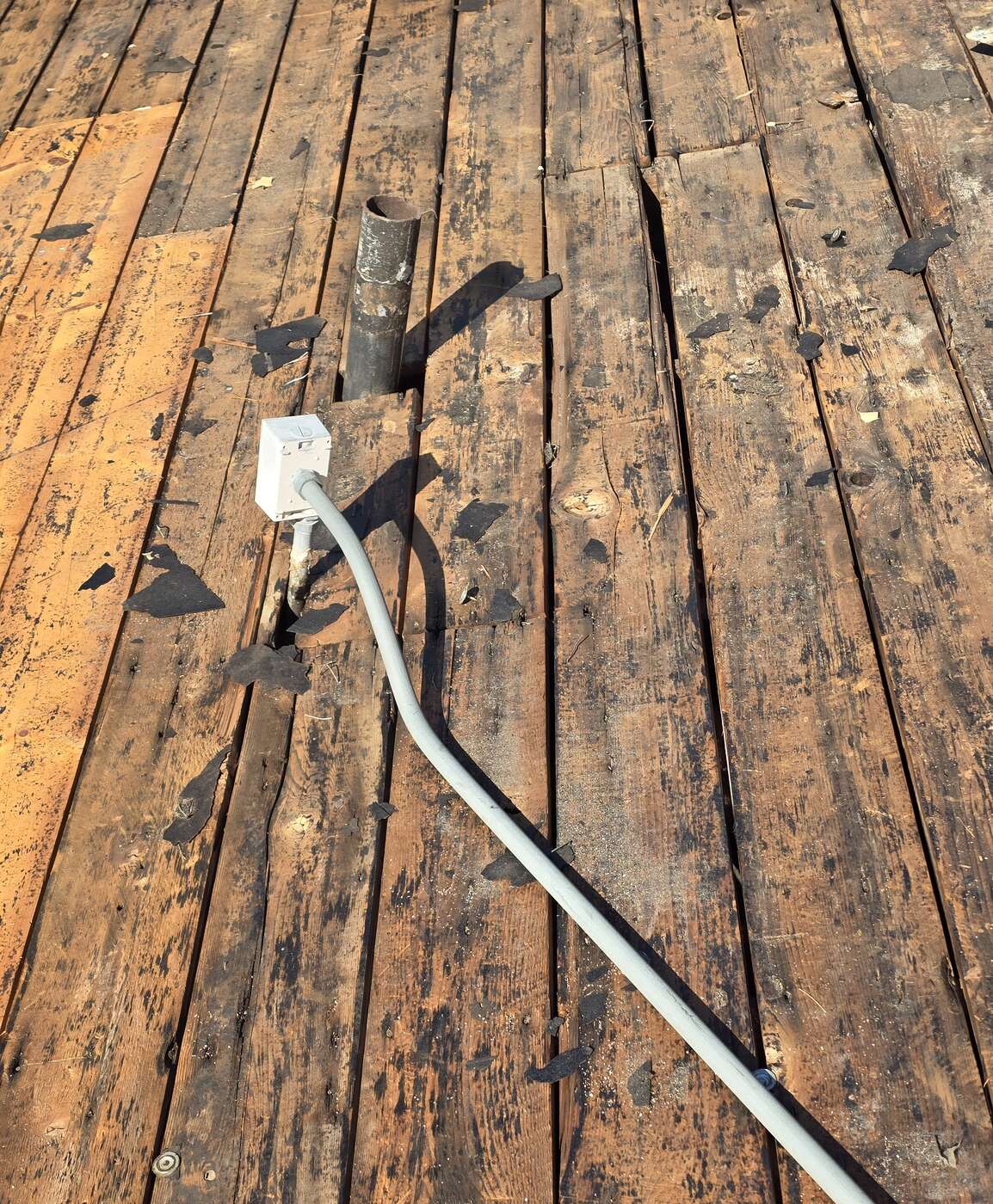 Old wood plank roof decking exposed after tear-off, with an electrical junction box and conduit running across the weathered boards.