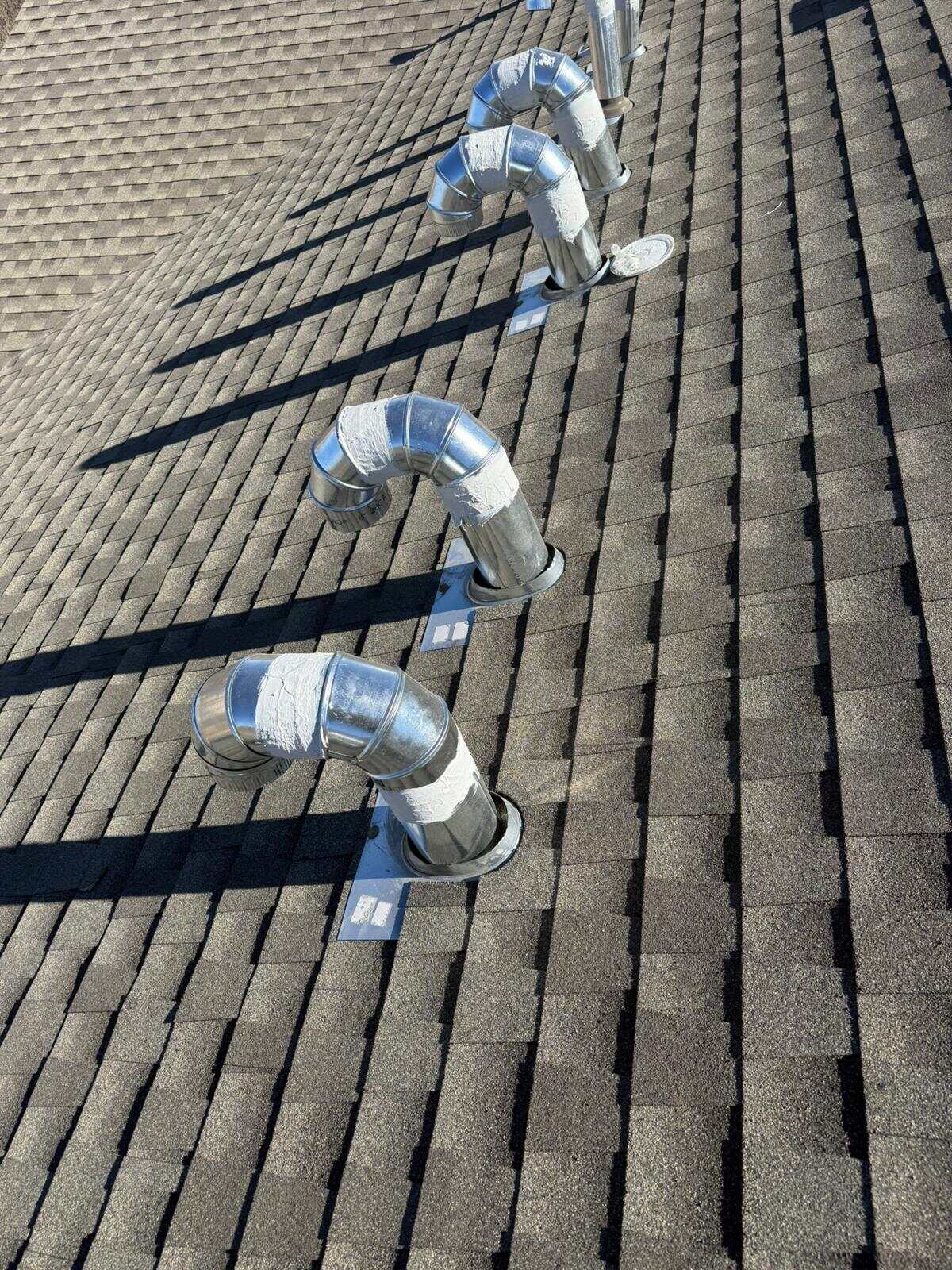 New galvanized duct elbows sealed with mastic stepping diagonally down a brown-gray shingle roof