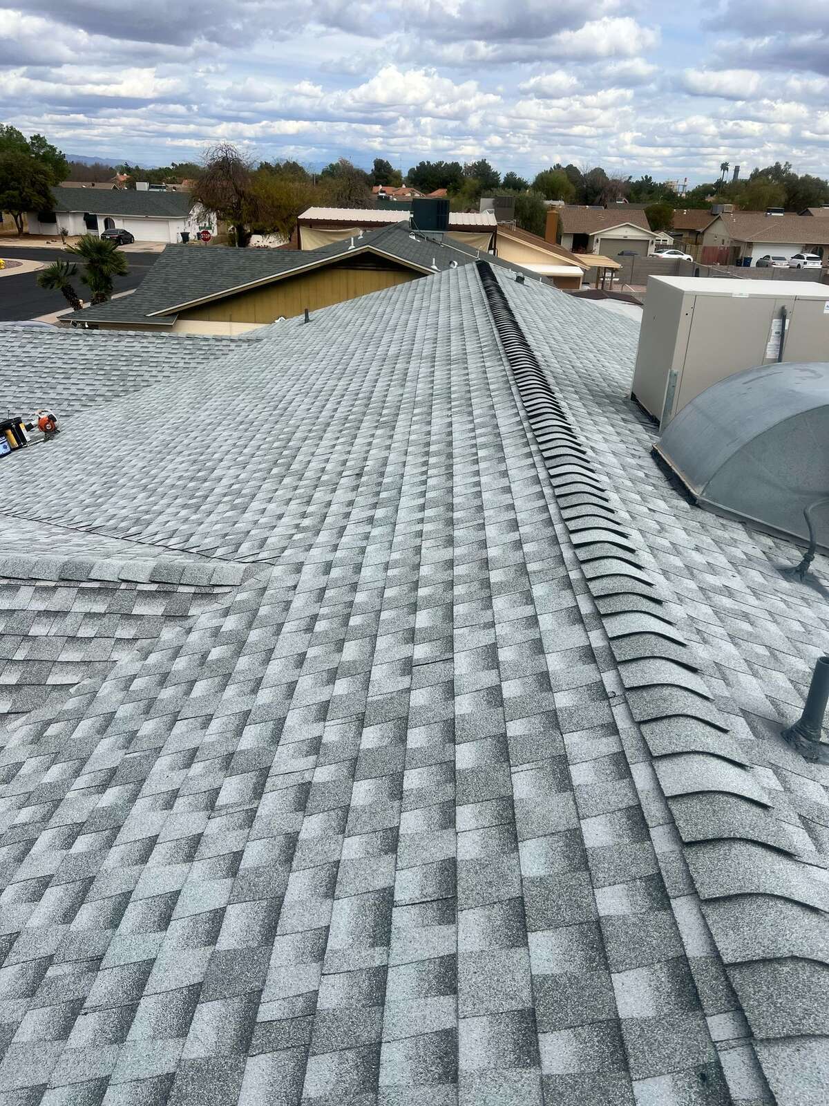 Freshly installed gray dimensional shingles across a hip roof with continuous ridge venting on a Phoenix home