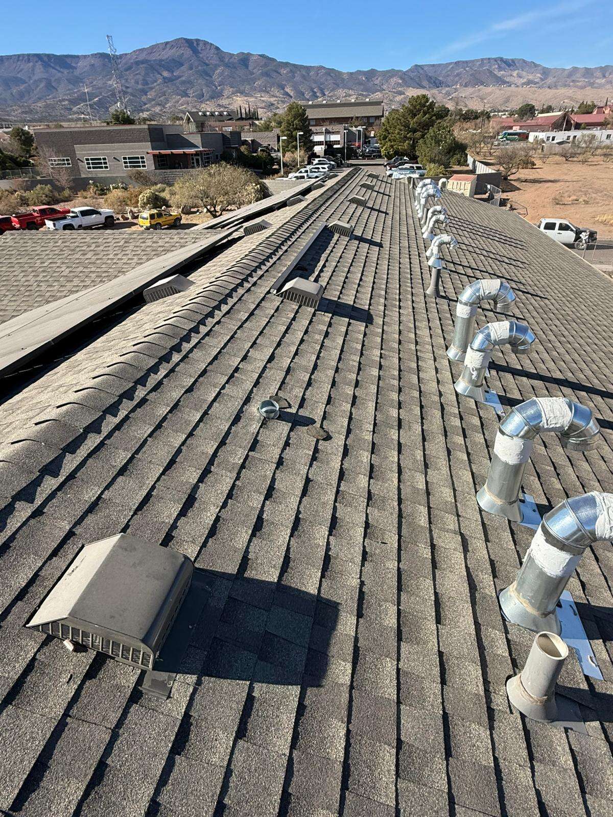 Long shingle roof lined with rows of new galvanized vents and box vents, mountains rising behind the town