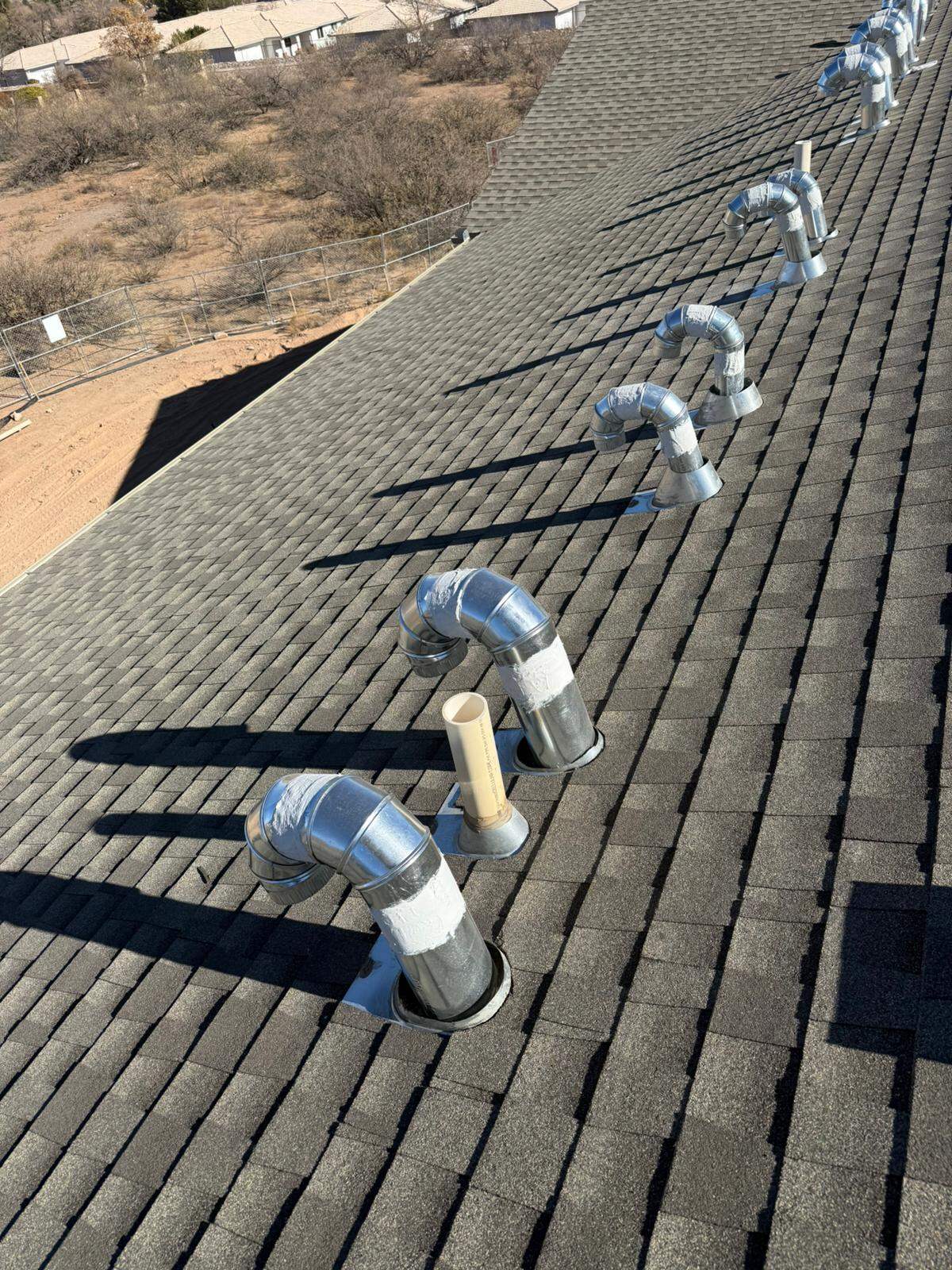 A long row of new galvanized roof vents receding up the slope of a large shingle roof