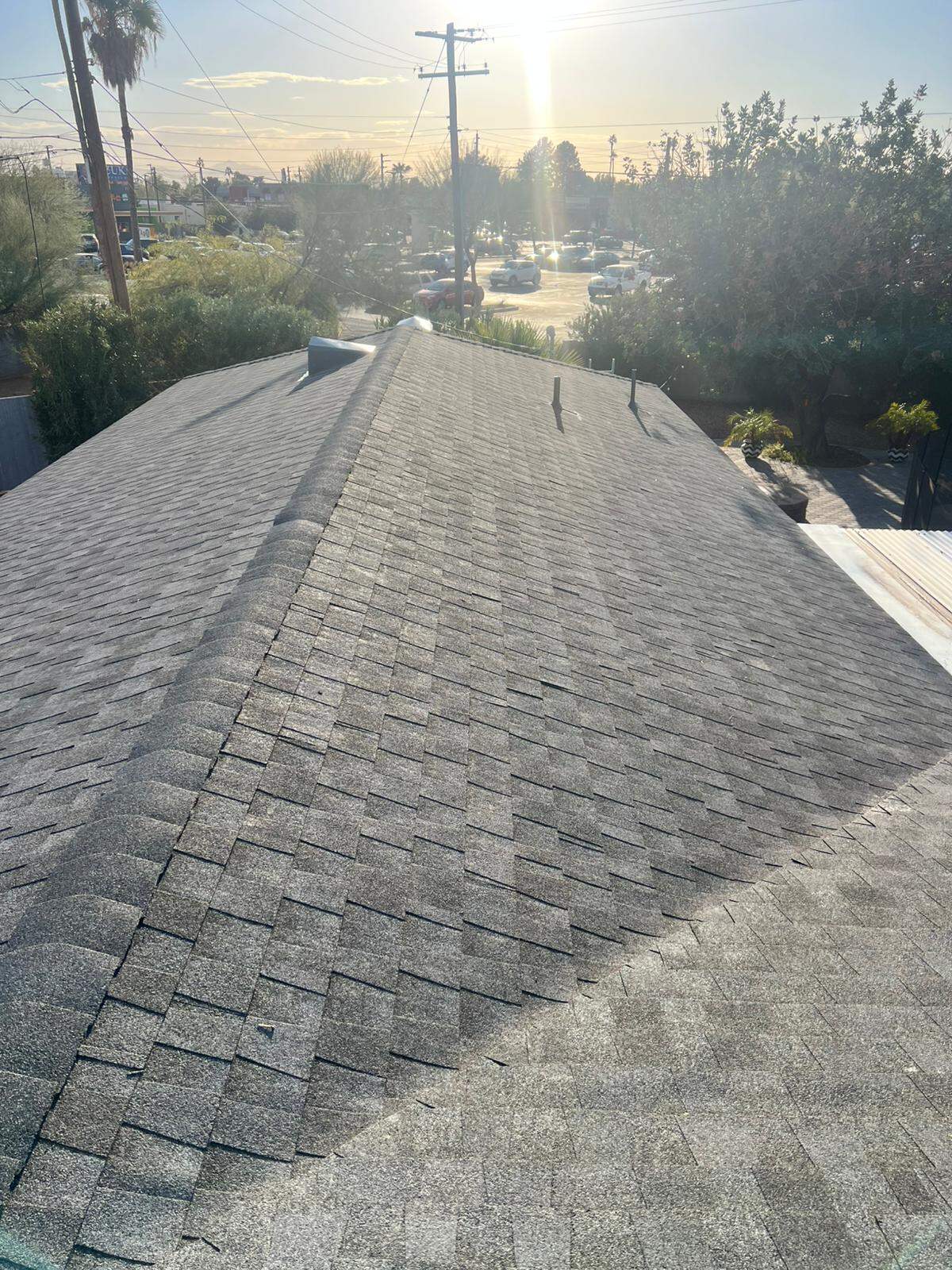 Weathered gray architectural shingle hip roof photographed from the ridge with a low sun behind