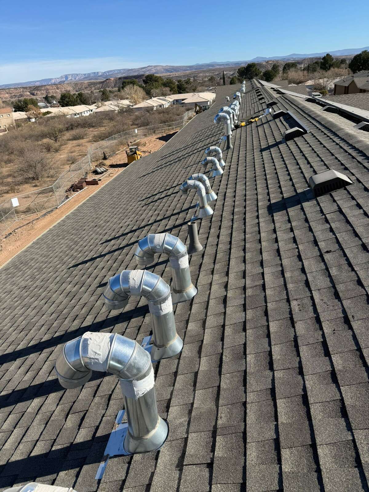 Wide view down a very long shingle roof lined with new vents, red-rock mesas on the horizon