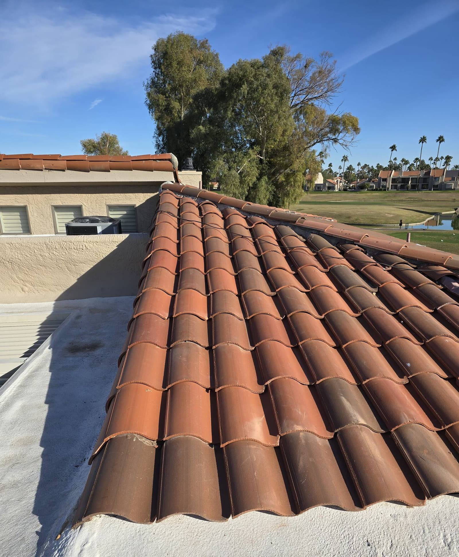 A long diagonal run of terracotta barrel tile on an Arizona roof, with a golf course, water hazard and palm trees stretching out behind it.