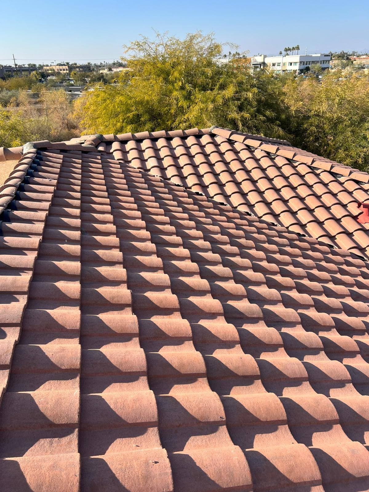 Rose-brown concrete S-tile roof planes meeting at a hip, with raking sunlight casting a repeating pattern of tile shadows