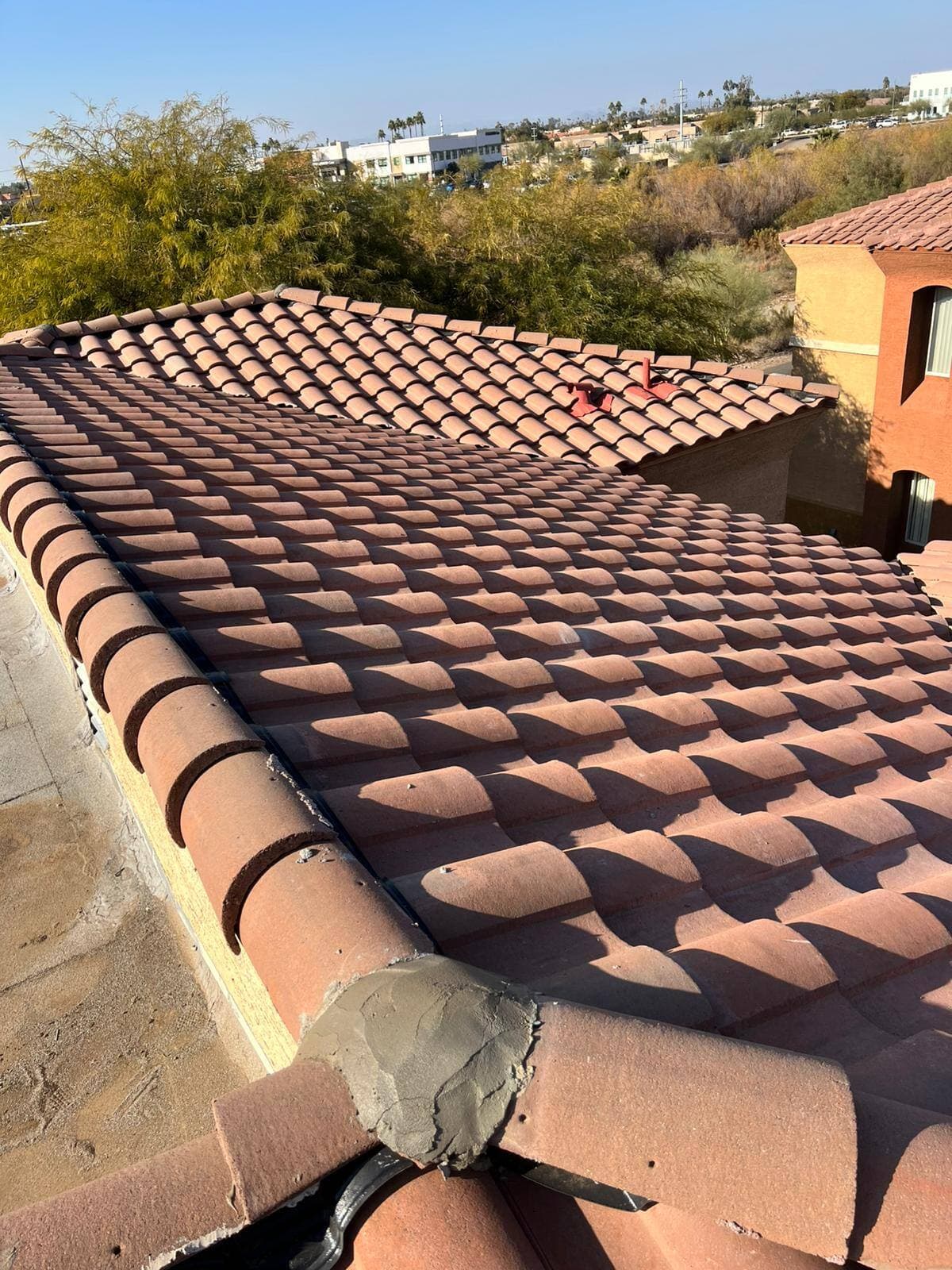 Concrete S-tile roof with mortared hip and ridge caps on a two-story stucco building under a clear Arizona sky