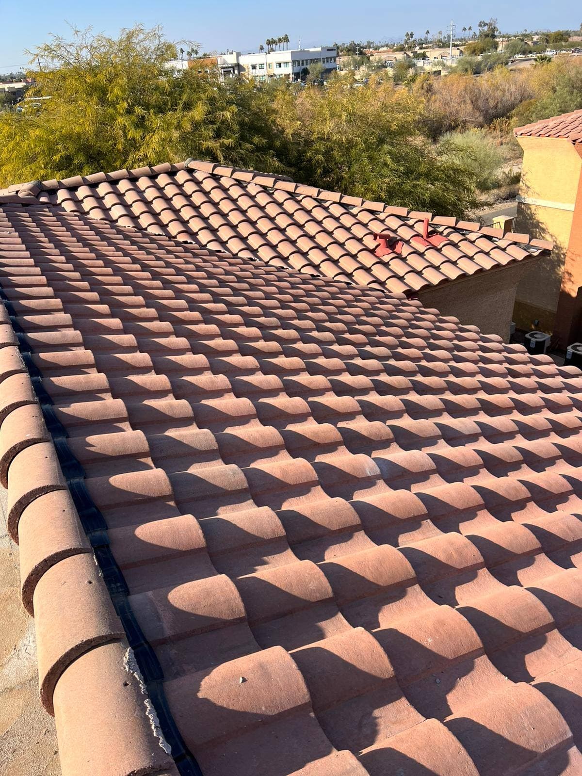 Finished two-tone terracotta barrel tile roof with deep shadow lines across every course, desert town beyond